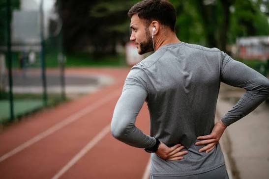 Male runner on an athletics track holding his lower back, illustrating disc and low back concerns