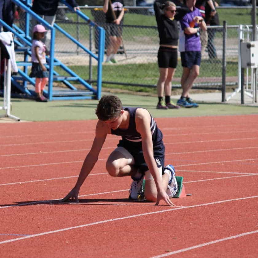 A young athlete kneeling on a running track, cared for at Farrelly Chiropractic in Narre Warren