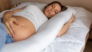 pregnant woman sleeping on her left side with a body pillow supporting her abdomen