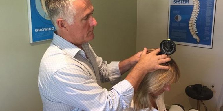 chiropractor measuring range of motion using an instrument placed on top a patient's head